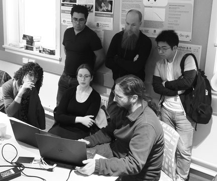 Mark in action, lower right, demonstrating data migration to RO-Crate. A black and white photograph of a group of people gathered round a computer.